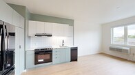 Located in Portland's vibrant SE Milwaukie Avenue neighborhood, this thoughtfully designed two-bedroom, two-bathroom residence offers a clean, modern aesthetic throughout. Light hardwood-style flooring runs continuously across the single-floor layout, lending warmth and visual continuity to every room.

The open kitchen is a standout feature, finished with sage-green lower cabinetry, crisp white upper cabinets, and a classic white subway tile backsplash. Black fixtures and hardware — including the range, dishwasher, and refrigerator — add a bold, contemporary contrast. The adjoining living area receives generous natural light through a large picture window with views of the surrounding neighborhood greenery.

Both bedrooms are bright and well-proportioned, with the primary bedroom offering direct access to its own bathroom, complete with a vanity featuring gray cabinetry and a white countertop. The second bathroom is equally well-finished, showcasing a tiled soaking tub and shower combination with matte black fixtures and a curved rod. Each bedroom includes an open closet with built-in shelving and hanging rods.

Throughout the unit, clean white walls, minimalist black hardware, and consistent flooring create a cohesive, modern atmosphere well-suited to comfortable urban living.