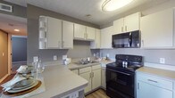 Located at 3793 Lakeview Trail in Canal Winchester, Ohio, this single-floor residence offers a practical and well-organized layout throughout. The kitchen is a standout feature, equipped with white cabinetry, ample counter space, a double-basin sink, and a full suite of black appliances including an electric range, over-the-range microwave, and refrigerator. A peninsula counter provides additional prep space and casual dining potential. The kitchen opens toward the entry door, creating a welcoming flow upon arrival, with wood-look flooring adding warmth underfoot. The bedrooms are carpeted and finished in neutral gray tones, each featuring closet storage — one with a sliding-door closet and another with a walk-in style closet. Textured ceilings are consistent throughout the home. The bathroom includes a tub-shower combination, a white built-in shelving unit for storage, and wood-look flooring. A dedicated laundry area accommodates a full-size washer and dryer with overhead wire shelving for added organization. A separate utility space houses the water heater and electrical panel, keeping mechanical systems neatly contained. The overall design is clean and neutral, offering a functional living environment in a residential Canal Winchester setting.