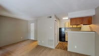 This single-floor studio offers a practical, open-concept layout that efficiently combines living and functional spaces. The main living area is finished with wall-to-wall carpeting in a neutral tan tone, creating a cohesive and understated aesthetic throughout. Large windows along the front wall allow natural light to flow freely into the space, offering views of the surrounding outdoor greenery and providing a bright, airy atmosphere. A front entry door is flanked by these windows, making the entryway feel welcoming and well-lit.

The kitchen is semi-enclosed, set slightly apart from the living area by a partial wall that serves as a natural divider. It features wood-toned cabinetry in both light and medium finishes, providing ample upper storage. The kitchen is equipped with a black refrigerator, a stainless steel single-basin sink with laminate countertops, and under-cabinet lighting. Wood-look flooring runs through the kitchen, distinguishing it from the carpeted living zone.

A closet with louvered doors provides convenient storage within the main living space. The bathroom includes a full-size soaking tub with a tiled surround in classic white, complemented by chrome fixtures. The textured ceiling is consistent throughout, adding a traditional residential character to the overall space.