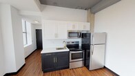 Located at 509 Market St in the heart of downtown Shreveport, Louisiana, this single-floor unit showcases an industrial-modern aesthetic that blends raw architectural elements with contemporary finishes. Exposed concrete columns and high ceilings contribute to the open, loft-inspired character of the space, while warm wood-tone flooring runs throughout, grounding the interior with a cohesive look.

The kitchen is a standout feature, outfitted with a two-tone cabinetry design — dark lower cabinets contrasted by crisp white upper cabinets, both accented with gold hardware. A white quartz countertop, undermount sink with a gold faucet, and a full suite of stainless steel appliances, including a refrigerator, electric range, and over-the-range microwave, complete the functional and stylish cooking space.

The open living area is generously proportioned, bathed in natural light streaming through large windows that frame views of the surrounding downtown Shreveport skyline. A bold black interior door adds a modern design accent throughout the unit.

The bathroom continues the contemporary theme with dark cabinetry, gold hardware, a white countertop vanity, wood-tone flooring, and a glass-enclosed standing shower, creating a clean and refined finish.