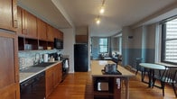 Located in the heart of Chicago's Loop at 159 N Wabash Ave, this single-floor unit offers a thoughtfully designed open-concept layout finished with warm bamboo hardwood flooring throughout the main living areas. The kitchen is well-appointed with rich wood cabinetry, granite countertops, a tile backsplash, full-size black appliances, and a central island with seating—ideal for both cooking and casual dining. Track lighting overhead enhances the kitchen's functionality and warmth.

The open living area flows seamlessly from the kitchen, featuring two-tone gray walls, large windows framing urban Chicago skyline views, and space for a comfortable seating arrangement centered around a marble-topped coffee table. A dedicated dining area adds further versatility to the layout.

Both bedrooms feature bold geometric-patterned accent walls, plush carpeting, ample closet storage, and windows that draw in natural light with city views. The primary bathroom includes a vessel sink vanity, white tile flooring, a glass-enclosed shower, and a large window offering striking skyline panoramas. A second full bathroom provides a vessel sink vanity and tiled shower, finished in a clean, neutral palette throughout.