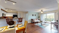 Located at 3641 SW Coquina Cove Way in Palm City, Florida, this well-appointed single-floor residence offers a comfortable and cohesive living experience with a coastal-inspired aesthetic throughout. The open-concept layout connects the living, dining, and kitchen areas seamlessly, all finished with warm hardwood flooring that adds a sense of continuity and warmth. The living room is bright and inviting, featuring a ceiling fan, textured ceilings, and a sliding glass door that opens to a private outdoor patio with serene waterfront views — a standout feature of the home. The kitchen is thoughtfully designed with white cabinetry, granite countertops, a breakfast bar with rattan bar seating, track lighting, and black appliances, including a full-size refrigerator and microwave. The dining area sits adjacent to the kitchen, making everyday meals and entertaining equally convenient. The bedroom offers plush carpeting, a soft accent wall, and a large window that frames peaceful water views, creating a tranquil retreat. A second carpeted room provides flexibility for use as a guest room or home office. Two full bathrooms are present, each featuring tub-shower combinations and granite-topped vanities. This home offers a calm, Florida-lifestyle ambiance with functional design throughout.