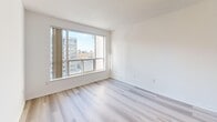 This efficiently designed one-bedroom, one-bathroom unit makes excellent use of its compact footprint across a single floor. Light-toned hardwood flooring runs throughout the main living areas, creating a bright and cohesive feel, while large windows throughout the unit frame urban city views and flood the space with natural light.

The living room benefits from generous window coverage, offering sweeping views of the surrounding cityscape. The kitchen features warm honey-toned cabinetry, a dark granite peninsula countertop, track lighting, a double sink, and full-sized white appliances including a refrigerator, stove, and built-in microwave — all finished with classic ceramic tile flooring.

The hallway connects the main living areas and includes a dedicated in-unit laundry closet with a stacked washer and dryer, a practical and convenient feature. The bedroom is a well-proportioned, bright room with large windows overlooking the city and a full-width sliding-door closet for ample storage.

The bathroom is finished with light ceramic tile flooring, a white vanity with storage, a mirrored medicine cabinet, and a full tub-shower combination with tile surround. Clean white walls throughout the unit contribute to an airy, move-in-ready ambiance.