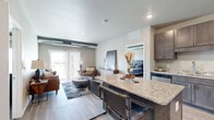 This well-appointed 2-bedroom, 3-bathroom residence in Aberdeen, SD offers a thoughtfully designed single-floor layout that maximizes both comfort and functionality. The open-concept living and kitchen area serves as the heart of the home, where light wood-style flooring flows seamlessly throughout. The kitchen is outfitted with rich dark-toned cabinetry, granite countertops, stainless steel appliances, and a spacious breakfast bar with seating — ideal for casual dining or entertaining. The living room is bright and inviting, featuring large sliding glass doors that open onto a private balcony overlooking lush outdoor scenery, allowing natural light to fill the space. Exposed ductwork adds an industrial design touch to the living area. Both bedrooms are carpeted and offer a calm, neutral palette, with the primary bedroom providing generous proportions and convenient closet access. The three bathrooms are finished with granite-topped vanities, dark cabinetry, and wood-style flooring, with at least one bathroom featuring an accessible walk-in shower with grab bars. Two dedicated closets provide ample storage throughout the residence. The overall ambiance is modern and comfortable, combining contemporary finishes with a warm, livable aesthetic.