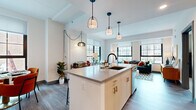 This thoughtfully designed 1-bedroom, 2-bathroom residence offers a functional and stylish single-floor layout. The open-concept living, dining, and kitchen area serves as the heart of the home, bathed in natural light from large, grid-paned windows that frame urban views. The living room features wide-plank hardwood flooring and generous wall space, while the dining area accommodates a full-sized table beside a bright window. The kitchen is fitted with light wood cabinetry, gold-toned hardware, a subway tile backsplash, and a full suite of stainless steel appliances. A dedicated office provides a quiet workspace, and the hallway connects all areas seamlessly with wood-look flooring and clean white walls accented by bold gray-blue doors. The bedroom offers a cozy retreat with a stylish sliding barn door leading to a walk-in closet. Two well-appointed bathrooms include white vanities with modern fixtures, large mirrors, and tiled finishes — one featuring a glass-enclosed walk-in shower with brushed gold hardware. The overall aesthetic balances contemporary design with warm, livable touches throughout.