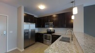 This single-floor kitchen is designed with a clean, contemporary aesthetic that balances style and functionality. The space is anchored by rich, dark espresso-toned cabinetry that extends from floor to ceiling, providing generous storage throughout. The upper and lower cabinets are fitted with sleek bar-style hardware, contributing to a streamlined, modern look.

Stainless steel appliances, including a French door refrigerator with an in-door ice and water dispenser, a range with an electric cooktop, and an over-the-range microwave, are seamlessly integrated into the cabinetry. The appliances offer both a cohesive visual appeal and practical utility.

Light granite countertops with subtle veining provide a striking contrast against the dark cabinetry, and this material is carried across the kitchen, including an extended peninsula or breakfast bar area that adds additional prep and dining space. A stainless steel undermount sink with a modern arc-neck faucet is positioned near a window, enhancing functionality.

A white subway tile backsplash adds texture and brightness to the space, while light hardwood-style flooring and pendant lighting overhead contribute to an inviting, well-lit atmosphere throughout.