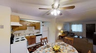 This single-floor, 2-bedroom, 2-bathroom residence offers a practical and welcoming layout designed for everyday comfort. The heart of the home is an open-concept kitchen and dining area, where warm wood cabinetry with raised-panel detailing provides ample storage alongside white appliances, including a refrigerator, dishwasher, and range. A double-basin sink sits beneath wall-mounted cabinetry, keeping the kitchen both organized and efficient. The adjacent dining space comfortably accommodates a dining table and chairs, with a ceiling fan overhead adding to the room's functionality and airflow. The open sightlines connect the dining area seamlessly to the living room, which features carpeted flooring, neutral walls, and windows that allow natural light to filter in. The living room offers generous space for seating arrangements, creating a relaxed and inviting atmosphere. A textured popcorn ceiling is present throughout, consistent with the home's classic residential character. The layout flows intuitively from room to room, making the space feel cohesive and easy to navigate. With its warm tones, functional design, and comfortable proportions, this residence provides a solid foundation for a variety of living arrangements.
