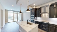 Located on the 10th floor at 500 West Trade Street in the heart of Charlotte, NC, this well-appointed one-bedroom, two-bathroom residence offers a refined urban living experience. The open-concept kitchen and living area serves as the centerpiece of the home, showcasing dramatic dark cabinetry with gold hardware, a large waterfall-edge quartz island with pendant lighting, white subway tile backsplash, stainless steel appliances, and a stainless range hood. Wood-look flooring flows throughout, complementing the warm, neutral palette. The living area opens to floor-to-ceiling sliding glass windows that flood the space with natural light and frame sweeping views of the Charlotte skyline and surrounding cityscape. The spacious primary bedroom continues the large-window theme, offering additional city views and direct access to the en-suite bathroom. The primary bath is elegantly finished with dark cabinetry, gold fixtures, marble-look tile flooring, and a glass-enclosed walk-in shower featuring white marble-style tile walls, a built-in bench, and matte black fixtures. A dedicated walk-in closet provides ample built-in shelving and hanging storage. A second full bathroom and hallway areas complete this thoughtfully designed urban residence.