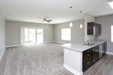This single-floor unit offers a well-designed layout with a cohesive neutral color palette of warm greige tones, white trim, and plush wall-to-wall carpeting throughout the living and bedroom areas. The open-concept living space is generously sized, equipped with a ceiling fan and light fixture, and benefits from natural light through a large window. A sliding glass door in one area of the living space provides outdoor access and views of the surrounding neighborhood.

The kitchen is positioned adjacent to the living area and features an island with granite countertops, rich dark-stained cabinetry, stainless steel appliances including a refrigerator, electric range, and over-the-range microwave, plus wood-look vinyl flooring. Pendant lighting and recessed fixtures add functional illumination.

The bedrooms are carpeted and feature neutral walls, ample outlets, and windows with blinds for privacy and natural light. The bathroom continues the dark cabinetry and granite countertop design, complemented by wood-look vinyl flooring. A notable feature is the in-unit stacked washer and dryer, conveniently located within the bathroom or adjacent utility space, adding significant practical value to the unit.