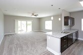 This single-floor unit offers a well-designed layout with a cohesive neutral color palette of warm greige tones, white trim, and plush wall-to-wall carpeting throughout the living and bedroom areas. The open-concept living space is generously sized, equipped with a ceiling fan and light fixture, and benefits from natural light through a large window. A sliding glass door in one area of the living space provides outdoor access and views of the surrounding neighborhood.

The kitchen is positioned adjacent to the living area and features an island with granite countertops, rich dark-stained cabinetry, stainless steel appliances including a refrigerator, electric range, and over-the-range microwave, plus wood-look vinyl flooring. Pendant lighting and recessed fixtures add functional illumination.

The bedrooms are carpeted and feature neutral walls, ample outlets, and windows with blinds for privacy and natural light. The bathroom continues the dark cabinetry and granite countertop design, complemented by wood-look vinyl flooring. A notable feature is the in-unit stacked washer and dryer, conveniently located within the bathroom or adjacent utility space, adding significant practical value to the unit.