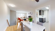 This thoughtfully designed single-floor residence offers a comfortable and functional layout across a well-utilized footprint. The open-concept living, dining, and kitchen area serves as the heart of the home, where warm hardwood flooring flows seamlessly throughout. The living room is bright and inviting, featuring a large window that fills the space with natural light, complemented by a ceiling fan and contemporary décor including a neutral sofa, bold accent chairs, and a round coffee table. The dining area accommodates a marble-topped table with upholstered chairs and enjoys its own window view. The galley-style kitchen is fully equipped with dark cabinetry, stainless steel appliances including a gas range, refrigerator, and built-in microwave, set against light countertops and large-format tile flooring, with a skylight providing additional brightness. The generously sized bedroom features hardwood floors, a window with natural light, and ample space for a queen bed and furnishings. The bathroom is clean and classic, featuring a full tiled tub-shower combination with chrome fixtures and a window for ventilation. A hallway and closet complete the layout, offering practical storage and circulation throughout the residence.
