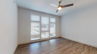 This well-designed single-floor residence offers a clean, contemporary aesthetic throughout. The main living area is bright and open, bathed in natural light streaming through a large bank of windows fitted with white horizontal blinds. A modern ceiling fan with a built-in light fixture anchors the space, while warm wood-look flooring extends seamlessly across the room, adding texture and visual warmth to the neutral white walls.

The galley-style kitchen is a functional highlight, featuring dark espresso cabinetry with brushed nickel hardware, white quartz countertops, a undermount stainless steel sink, and a full suite of stainless steel appliances, including a refrigerator, microwave, and dishwasher. A classic subway tile backsplash adds a refined finishing touch.

Additional rooms continue the consistent use of wood-look flooring, crisp white walls, and natural light, offering versatile and well-proportioned spaces. Doorways are framed with classic panel-style doors in white, contributing to the home's cohesive design language.

The bathroom features matching dark cabinetry with a white quartz vanity top, an undermount sink with a brushed nickel faucet, and tile flooring. A laundry area with additional storage cabinetry is conveniently accessible from the bathroom. Overall, the space presents a polished, modern living environment with consistent finishes and thoughtful details throughout.