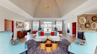 Located at 140 Bromley Village Drive in Fort Mill, SC, this single-floor community space is a masterfully designed gathering hub that blends bold color with refined architectural details. The centerpiece is a grand living room anchored by a soaring vaulted ceiling adorned with a statement sputnik chandelier. Herringbone-patterned hardwood floors flow throughout, lending warmth and visual interest to the entire space. Large windows and glass French doors bathe the room in natural light while offering views of the outdoors, complemented by elegant floor-length drapes. Vibrant teal wingback chairs, crisp white sofas, and vivid red and turquoise accent pillows create a lively, welcoming atmosphere. A cozy lounge nook features a bold teal accent wall, globe pendant lighting, and colorful framed artwork, offering an intimate retreat within the larger space. Glass-paneled sliding doors provide a seamless connection to an adjacent room. The kitchen area is defined by a textured reclaimed wood accent wall, dark cabinetry with gold hardware, a generous white quartz island with bar seating, globe pendant lights, and dual wall-mounted TVs — making it an ideal social and entertainment hub. Every detail reflects a thoughtful, design-forward aesthetic.