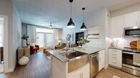 This thoughtfully designed single-floor residence offers a seamless blend of modern style and everyday functionality. The open-concept kitchen is a standout feature, anchored by a granite-topped island with an integrated farmhouse-style stainless steel sink and seating for two. White shaker cabinetry, a subway tile backsplash, and a full suite of stainless steel appliances — including a French door refrigerator, range, built-in microwave, and dishwasher — complete the space. Pendant lighting adds a contemporary touch overhead. The kitchen flows naturally into the living area, which is filled with natural light from oversized French doors that open to a balcony, complemented by a ceiling fan and warm hardwood-style flooring. The living room offers a relaxed, modern ambiance with neutral tones and clean lines. Two bedrooms provide comfortable retreats, each carpeted and appointed with large windows that bring in abundant natural light and views of the surrounding area. The full bathroom is generously sized, featuring a dual-sink vanity with granite countertops, ample white cabinetry, large-format tile flooring, and a soaking tub with a tiled surround. Throughout the residence, a cohesive neutral palette and quality finishes create an inviting, polished atmosphere.