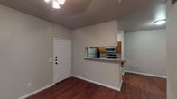 This single-story residence offers a functional and straightforward layout designed for comfortable everyday living. The main living area features rich, dark wood-style flooring that extends through the entry, living space, and into the kitchen corridor. A ceiling fan overhead provides both light and airflow, while a sliding glass door dressed with vertical blinds allows natural light to fill the space.

The galley-style kitchen is well-equipped, featuring warm medium-toned wood cabinetry, granite-look countertops, and stainless steel appliances including a refrigerator, electric range, and over-the-range microwave. A double-basin sink and dishwasher add to the kitchen's practicality. A pass-through breakfast bar connects the kitchen to the living area, and a dedicated pantry closet provides additional storage. The kitchen opens toward the living space, creating a connected flow throughout the common areas.

The bedrooms are carpeted for comfort, each featuring ceiling fans with light fixtures and windows fitted with horizontal blinds that allow natural light in. One bedroom includes a roomy reach-in closet. The bathroom is clean and simple, featuring a full-size soaking tub with a tiled tub surround and a shower rod, complemented by wood-style flooring.