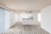 This single-floor unit offers a clean, functional layout with an open-concept design connecting the living area and kitchen. The living space is finished with light wood-style laminate flooring and features large vertical-blind-covered sliding doors that draw in generous natural light. A textured ceiling runs throughout the unit, adding a classic touch to the neutral, warm-toned walls.

The kitchen is anchored by a peninsula with a dark countertop and bar seating, making it ideal for casual dining or entertaining. White cabinetry provides ample storage, while a vibrant mosaic tile backsplash in blues, greens, and golds adds a pop of color. White appliances, including a refrigerator and electric range with overhead ventilation, complete the kitchen.

The bedrooms are well-proportioned, each with light wood flooring, baseboard heating, and windows overlooking lush greenery. One bedroom includes a sliding-door closet for convenient storage.

The unit includes two bathrooms. The full bathroom features a tiled tub surround, a vanity with a light countertop, and white cabinetry, while a second bathroom offers a vanity with a mirrored medicine cabinet. Both bathrooms are bright and efficiently designed. Baseboard heating is present throughout the unit.
