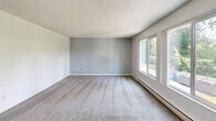 Located at 7900 NE Bothell Way in Kenmore, WA, this three-bedroom, two-bathroom residence offers a practical and well-organized single-floor layout. The galley-style kitchen features white cabinetry, laminate countertops, wood-style flooring, a double-basin sink, and white appliances including a refrigerator and electric range. The kitchen flows directly into the combined living area, which is brightened by a sliding glass door that opens to a private balcony and is complemented by a ceiling fan overhead. The living room continues the wood-style flooring and provides a comfortable, open feel. Each of the three bedrooms is carpeted and finished with neutral tones, textured ceilings, and baseboard heating. The bedrooms receive natural light through blinded windows, with the primary bedroom offering a notably spacious layout. The two bathrooms feature wood-style flooring, with one bathroom including a walk-in shower and grab bar, and the other offering a tub-shower combination with a single vanity and mirror. A hallway connects the living spaces to the private quarters. Throughout the unit, textured ceilings and clean white walls maintain a consistent and tidy aesthetic.
