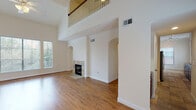 This three-story residence is defined by its dramatic double-height living room, where soaring ceilings open to an upper-level balcony with classic wood balusters. Warm hardwood flooring flows throughout the main level, complementing the neutral cream-toned walls and crisp crown molding. A tile-surround fireplace serves as a focal point, while arched architectural details and large windows with blinds allow ample natural light throughout.

The galley-style kitchen is well-appointed with rich cherry wood cabinetry, granite countertops, a stone tile backsplash, stainless steel appliances including a refrigerator, range, microwave, and dishwasher, and stone-look tile flooring. Built-in shelving and a dedicated desk area add functional detail to the adjacent hallway.

Bedrooms are carpeted and generously proportioned, with multiple windows providing natural light and ceiling fans for comfort. En-suite bathrooms feature granite or dark stone vanity tops, white cabinetry, tile flooring, and glass-enclosed showers or tub-shower combinations. Upper-level hallways with hardwood floors connect the staircase landing to additional bedrooms, reinforcing the home's cohesive, well-maintained aesthetic throughout all three levels.