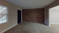 Located at 6100 Waters Ave in Savannah, Georgia, this single-floor unit offers a straightforward and functional layout across several well-defined living spaces. The living area greets residents with warm neutral-toned walls, wall-to-wall carpeting, and a front entry door that opens to a striking exposed brick accent wall, lending the space a distinctive, character-rich aesthetic. Natural light filters in through a window fitted with blinds, brightening the open feel of the room.

The bedrooms continue the neutral color palette with plush carpeting underfoot and ceiling fans with integrated lighting for year-round comfort. One bedroom features a bold terracotta accent wall paired with a pendant light fixture, adding a touch of visual interest. HVAC vents are present throughout for climate control.

The kitchen is equipped with white cabinetry, a double-basin stainless steel sink, laminate countertops, and a white electric range with overhead ventilation — providing all the essentials for everyday cooking. Vinyl flooring completes the practical design of this space.

The bathroom includes a full tub and shower combination surrounded by white square tile, complemented by a grab bar for added safety and convenience. Throughout the unit, clean lines, consistent finishes, and functional details make this a practical and comfortable living space in Savannah's 31406 area.
