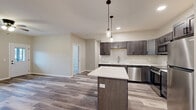 Located at 387 Chippewa Mall Dr in Chippewa Falls, WI, this thoughtfully designed one-bedroom, one-bathroom unit offers a comfortable and modern living experience on a single floor. The open-concept layout seamlessly connects the kitchen and living room, creating an inviting, efficient use of space. The kitchen is a standout feature, boasting dark espresso-toned shaker cabinets, crisp white countertops, a central island with pendant lighting overhead, and a full suite of stainless steel appliances including a dishwasher, range, microwave, and refrigerator. Light wood-tone luxury vinyl plank flooring flows throughout the main living areas, adding warmth and a contemporary feel. The spacious bedroom is finished with plush carpet, a ceiling fan, and a window that brings in natural light and outdoor views. The bathroom features a full soaking tub and shower combination with clean white surround. Additional conveniences include a dedicated laundry area and two closets for generous storage. A private entry door with an adjacent window and wall-unit climate control further enhance the unit's functionality. Neutral wall tones and recessed lighting throughout create a bright, clean ambiance well-suited for everyday living.