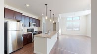 This well-appointed single-floor residence showcases a thoughtfully designed open-concept layout that seamlessly connects the kitchen, dining, and living areas. The kitchen is a standout feature, centered around a large island with granite countertops and an undermount sink, illuminated by stylish pendant lighting. Rich dark-wood cabinetry lines the walls and is complemented by a classic tile backsplash, while a full suite of stainless steel appliances — including a refrigerator, range, and microwave — provides modern functionality. Hardwood-style flooring flows throughout the main living areas, adding warmth and cohesion to the open floor plan. The spacious living room benefits from abundant natural light, courtesy of large windows and transom windows that draw the eye upward, with sliding glass door access adding to the airy feel. Bedrooms are finished with plush wall-to-wall carpeting, ceiling fans, and generously sized windows with blinds. The bathroom features dark cabinetry with a wide vanity, white countertops, a large mirror with vanity lighting, and hardwood-style flooring. A walk-in closet and additional storage spaces round out the practical amenities of this clean and contemporary residence.