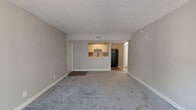 Located at 5959 Fort Caroline Rd in Jacksonville, Florida, this single-floor unit offers a well-organized layout designed for comfortable everyday living. The spacious living area is finished with soft gray carpeting and neutral-toned walls, creating a bright and airy atmosphere. Large windows dressed with vertical blinds allow generous natural light to fill the room, enhancing its open feel. A textured ceiling runs throughout the main living spaces, adding a classic residential touch.

The kitchen is accessible via a pass-through counter opening from the living area, providing a connected and functional flow. It features white shaker-style cabinetry with matte black hardware, a marble-patterned countertop, a double-basin stainless steel sink with a matte black faucet, and a subway tile backsplash. Black appliances, including a range, over-the-range microwave, refrigerator, and dishwasher, complete the space. Durable wood-look vinyl flooring runs throughout the kitchen.

The bathroom is clean and well-appointed, with a white vanity, matte black fixtures, a framed mirror with overhead lighting, wood-look vinyl flooring, and a full tub-shower combination. The bedroom offers plush gray carpeting, neutral walls, and a sliding door closet, providing a calm and functional retreat.