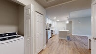 This thoughtfully designed single-floor residence offers a clean, modern aesthetic throughout its open-concept layout. Light wood-look flooring runs continuously across all rooms, creating a warm and cohesive feel. The kitchen is a standout centerpiece, featuring crisp white shaker cabinetry extending to the ceiling, a classic subway tile backsplash, white quartz countertops, and a full suite of stainless steel appliances including a refrigerator, range, and over-the-range microwave. A large kitchen island with a built-in sink and pendant globe lighting above serves as both a functional workspace and a natural gathering point. The open living area connects seamlessly to the kitchen, offering generous space illuminated by natural light from large windows and sliding glass doors, complemented by a ceiling fan overhead. The bedrooms are well-proportioned with neutral wall tones, ceiling fans, and windows that invite natural light. Storage is addressed with panel-style closet doors throughout. Two bathrooms are finished with wood-look tile flooring, white vanities, and tiled surrounds — one featuring a walk-in shower and the other a full soaking tub. An in-unit laundry area adds everyday convenience to this well-appointed space.