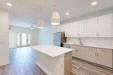 Located at 25 Silver Moon Circle in St. Augustine, FL, this thoughtfully designed one-bedroom, one-bathroom residence offers a clean, modern aesthetic throughout its efficiently organized single floor. The open-concept kitchen and living area serves as the heart of the home, featuring crisp white cabinetry extending to the ceiling, a white quartz-topped island with pendant lighting, and a full suite of stainless steel appliances including a refrigerator, range, microwave, and dishwasher. Wood-look plank flooring runs seamlessly throughout, complementing the bright, neutral color palette. The living area is appointed with a ceiling fan and opens to a private balcony through a glass-panel door, allowing natural light to pour in and offering outdoor views. The bedroom is a sun-filled retreat with large windows, wood-look flooring, and access to a spacious walk-in closet equipped with multi-tier wire shelving. A second closet provides additional storage. The bathroom features a white vanity with quartz countertop, gold-tone fixtures, large-format tile flooring, and a glass-enclosed shower with dark tile surround. A dedicated laundry area and utility room complete the functional layout of this well-appointed residence.