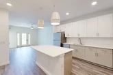 Located at 25 Silver Moon Circle in St. Augustine, FL, this thoughtfully designed one-bedroom, one-bathroom residence offers a clean, modern aesthetic throughout its efficiently organized single floor. The open-concept kitchen and living area serves as the heart of the home, featuring crisp white cabinetry extending to the ceiling, a white quartz-topped island with pendant lighting, and a full suite of stainless steel appliances including a refrigerator, range, microwave, and dishwasher. Wood-look plank flooring runs seamlessly throughout, complementing the bright, neutral color palette. The living area is appointed with a ceiling fan and opens to a private balcony through a glass-panel door, allowing natural light to pour in and offering outdoor views. The bedroom is a sun-filled retreat with large windows, wood-look flooring, and access to a spacious walk-in closet equipped with multi-tier wire shelving. A second closet provides additional storage. The bathroom features a white vanity with quartz countertop, gold-tone fixtures, large-format tile flooring, and a glass-enclosed shower with dark tile surround. A dedicated laundry area and utility room complete the functional layout of this well-appointed residence.