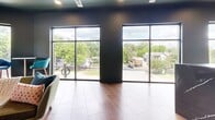 Located at 661 Wedgewood Ave in Nashville, TN, this single-floor amenity space spans a generously sized footprint and delivers a dynamic blend of function and style. The fitness center is a standout feature, boasting bold navy and blue walls, rubberized flooring, and a comprehensive array of equipment including cable machines, treadmills, stationary bikes, and free weights. Floor-to-ceiling windows and sliding glass doors flood the workout area with natural light and provide views of the surrounding outdoor space. Adjacent to the gym, a dedicated cardio and stretching zone offers additional versatility for varied workout routines. The social and lounge areas showcase an eclectic, curated design aesthetic, with warm mauve and moody charcoal walls, checkered tile flooring, and richly upholstered seating. A cozy lounge nook features a wraparound caramel leather sectional, globe sconces, and a welcoming, intimate atmosphere. The kitchen and bar area is anchored by a striking dark marble island with bold white veining, complemented by yellow cabinetry, open shelving with brass-toned lighting, and warm terracotta tile floors. Oversized windows throughout the communal spaces frame neighborhood views, enhancing the bright and inviting ambiance of this thoughtfully appointed Nashville retreat.