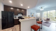 This two-story residence offers a thoughtfully designed layout that balances open communal spaces with private retreats. The kitchen serves as a central hub, featuring rich dark-brown cabinetry, light countertops, black appliances including a French door refrigerator and electric range, and a peninsula with bar seating. Wood-look flooring flows seamlessly from the kitchen into the living area, which is bathed in natural light from sliding glass doors opening to a private balcony with outdoor views. A statement chandelier adds a refined touch overhead.

Multiple bedrooms are distributed across both floors, each finished with the same wood-look flooring, neutral walls, and windows that invite natural light. One upper-level room features vaulted ceilings, adding an airy, elevated feel to the space. The bathrooms are a standout feature, finished with striking marble-style tile surround walls. One bathroom includes a walk-in shower, while the other offers a full soaking tub. Both share the consistent dark-wood vanity cabinetry and light countertop pairing found throughout the home, creating a cohesive and polished aesthetic overall.
