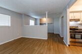 Located at 11405 Colorado Ave in Kansas City, MO, this single-story unit offers a straightforward, functional layout with consistent hardwood-style flooring running throughout the main living areas. The open floor plan connects the living space to the kitchen, creating a cohesive and practical flow. A half-wall partition defines separate zones within the open area while maintaining a sense of spaciousness. Multiple windows dressed with horizontal blinds allow natural light to filter into the living spaces, brightening the neutral gray walls and textured ceilings.

The kitchen is equipped with a black electric range, an overhead ventilation hood, and ample upper cabinetry in white with bar-pull hardware. Dark speckled countertops provide generous workspace and contrast neatly with the light cabinetry. The layout makes efficient use of the available space for cooking and storage.

The bathroom features a tiled tub-shower combination, a single vanity with a light countertop, and a mirror. Textured walls and hardwood-style flooring carry through into this space as well, maintaining a cohesive aesthetic. An open closet area with a hanging rod is visible in the main living zone, offering accessible storage. Overall, the space presents a clean, move-in ready environment with practical amenities.