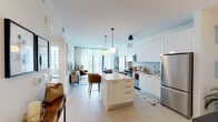 This contemporary high-rise residence is designed with a clean, modern aesthetic throughout its single-floor layout. The open-concept living and dining area flows seamlessly into a well-equipped kitchen, creating a bright and connected living space. Floor-to-ceiling windows and sliding glass doors flood the interior with abundant natural light while framing expansive city skyline views. A private balcony accessible from the living area extends the living space outdoors.

The kitchen is a standout feature, outfitted with high-gloss white cabinetry that extends to the ceiling, a textured penny-tile backsplash, stainless steel appliances including a range, microwave, dishwasher, and French door refrigerator, and a generous quartz-topped island with pendant globe lighting overhead.

Two bedrooms each offer direct access to a private balcony via floor-to-ceiling sliding glass doors, delivering sweeping urban panoramas. Both rooms feature ample closet storage and are bathed in natural light.

Two bathrooms serve the residence. The primary bathroom features dark warm-toned wall tile, a glass-enclosed walk-in shower, a dual-sink white vanity with quartz countertops, and a large mirror with globe sconce lighting. The secondary bathroom presents a crisp all-white design with an undermount sink, white cabinetry, and a full-width mirror. Light-toned flooring runs throughout the residence, tying the spaces together cohesively.