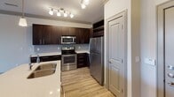 This single-floor residence offers a thoughtfully designed open-concept layout that seamlessly connects the living and kitchen areas. The main living space features warm light hardwood-style flooring, crown molding, and flush-mount ceiling lighting that creates a bright, welcoming atmosphere throughout.

The kitchen is a standout feature, showcasing rich dark espresso cabinetry, a subway tile backsplash, and a full suite of stainless steel appliances including a refrigerator, electric range, and microwave. A central island with a light quartz countertop and an undermount sink serves as both a functional workspace and a natural gathering point. Pendant and track lighting above the island and counters add a modern, polished touch. A dedicated pantry closet provides ample additional storage.

The bedrooms offer a comfortable contrast with plush carpeting underfoot and windows fitted with horizontal blinds that allow for adjustable natural light. Crown molding carries throughout, lending a cohesive, refined character to each room. One bedroom features a ceiling fan for added comfort.

Overall, the space presents a clean, modern aesthetic with a practical floor plan, quality finishes, and a neutral palette that provides a versatile backdrop for a variety of living arrangements.