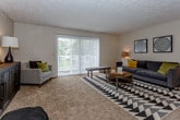 This single-floor residence offers a thoughtfully designed open-concept layout that seamlessly connects the living, dining, and kitchen areas. The spacious living room is a welcoming focal point, featuring plush carpeting, a textured ceiling, and a large sliding glass door dressed with vertical blinds that floods the space with natural light and provides access to outdoor views. A bold geometric area rug and warm ambient lighting contribute to the room's inviting character.

The dining area flows naturally from the living space and is outfitted with a ceiling fan overhead. Floating shelves and decorative wall art add a personalized touch to the neutral walls.

The kitchen is designed for functionality, featuring warm wood cabinetry, white countertops, hardwood-style flooring, and black appliances including a range and refrigerator. Overhead lighting ensures the space is well-lit for meal preparation.

The bedrooms are carpeted and serene, with textured ceilings and windows that bring in natural light. The primary bedroom benefits from generous closet space with built-in organization, while additional bedrooms offer ample room and storage.

The bathroom is clean and practical, featuring a vanity with dark wood cabinetry, a tiled tub-shower combination with a curtain, and hardwood-style flooring. Neutral tones throughout the home create a calm, cohesive ambiance.