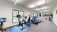 Located at 105 Laurel Hill Rd in Brookfield, CT, this well-appointed fitness center offers a thoughtfully designed single-floor exercise space ideal for a comprehensive workout experience. The room is finished with durable speckled rubber flooring throughout, providing both safety and functionality underfoot.

The space is divided into distinct functional zones. The cardio area is equipped with multiple treadmills, elliptical machines, a stationary spin bike, and a rowing machine, all positioned along a wall of large, grid-pane windows that flood the room with natural light and offer refreshing views of the surrounding greenery. A full-length mirror along one wall visually expands the space and supports form-checking during exercise.

The free weights zone features a multi-tier dumbbell rack with a wide range of weights, accompanied by adjustable workout benches, offering ample options for strength training routines.

A striking feature wall anchors one end of the room, displaying a topographic mountain mural alongside the motivational phrase "KEEP CLIMBING" in bold orange lettering — setting an energizing tone throughout. Linear LED pendant lighting runs the length of the ceiling, providing bright, even illumination that complements the natural light from the windows.

The clean white walls, modern finishes, and open layout make this fitness center a functional and inspiring environment for all levels of fitness enthusiasts.