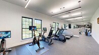 Located at 105 Laurel Hill Rd in Brookfield, CT, this well-appointed fitness center offers a thoughtfully designed single-floor exercise space ideal for a comprehensive workout experience. The room is finished with durable speckled rubber flooring throughout, providing both safety and functionality underfoot.

The space is divided into distinct functional zones. The cardio area is equipped with multiple treadmills, elliptical machines, a stationary spin bike, and a rowing machine, all positioned along a wall of large, grid-pane windows that flood the room with natural light and offer refreshing views of the surrounding greenery. A full-length mirror along one wall visually expands the space and supports form-checking during exercise.

The free weights zone features a multi-tier dumbbell rack with a wide range of weights, accompanied by adjustable workout benches, offering ample options for strength training routines.

A striking feature wall anchors one end of the room, displaying a topographic mountain mural alongside the motivational phrase "KEEP CLIMBING" in bold orange lettering — setting an energizing tone throughout. Linear LED pendant lighting runs the length of the ceiling, providing bright, even illumination that complements the natural light from the windows.

The clean white walls, modern finishes, and open layout make this fitness center a functional and inspiring environment for all levels of fitness enthusiasts.