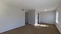 This single-story residence offers a practical and functional layout across several well-defined spaces. The living area is spacious and open, finished with neutral-toned carpet and light gray walls beneath a textured ceiling. A distinctive arched window allows natural light to filter in, creating bright patches across the floor. A central wall divides the living space from adjacent areas, providing a sense of structure while maintaining an open feel.

The kitchen features white cabinetry both above and below dark granite-style countertops, complemented by a stainless steel sink and a full-size refrigerator. Wood-look flooring runs throughout the kitchen, offering a clean contrast to the carpeted areas of the home.

Two bathrooms serve the residence. One includes a tub-shower combination with large beige wall tiles, a granite-top vanity with white cabinetry, and wood-look flooring. The second bathroom offers a similar vanity design in a more compact layout, with a wall-mounted light fixture and a louvered ventilation panel.

The bedrooms are carpeted and finished with the same gray walls and textured ceilings found throughout. Each room includes a ceiling fan with a light fixture and an arched window that provides natural light and outdoor views. The overall ambiance of the space is clean, neutral, and move-in ready.