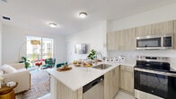 Located at 1150 SW 70th Avenue in Miami, FL, this well-appointed one-bedroom, one-bathroom residence offers a thoughtfully designed open-concept layout with clean, modern finishes throughout. Gleaming light-toned tile floors and crisp white walls create a bright, airy atmosphere that flows seamlessly from room to room.

The living area is inviting and functional, featuring a sliding glass door that opens to a private balcony, flooding the space with natural light and providing outdoor views. The kitchen is a standout feature, showcasing light wood cabinetry, white quartz countertops, stainless steel appliances — including a refrigerator, range, microwave, and dishwasher — and a peninsula with bar seating, ideal for casual dining or entertaining.

The bedroom is a serene retreat, benefiting from a large window that draws in abundant natural light and offers pleasant outdoor views. Three closets throughout the unit provide generous storage options. The bathroom is finished with a wood-tone vanity, a large mirror, and a shower-tub combination. Additional conveniences include an in-unit laundry area and a connecting hallway that ties the layout together efficiently. This residence combines practical design with a fresh, contemporary aesthetic in a prime Miami location.