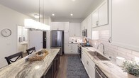 This thoughtfully designed single-floor residence offers a cohesive blend of modern finishes and functional living spaces. The kitchen stands out with crisp white shaker cabinetry, granite countertops, a subway tile backsplash, stainless steel appliances including a gas range, built-in microwave, refrigerator, and dishwasher, along with a large center island ideal for dining or meal prep. Wood-look flooring runs throughout the main living and kitchen areas, adding warmth and continuity.

The living room is bright and welcoming, featuring sliding glass doors that open to a private balcony, allowing natural light to fill the space. Neutral walls provide a versatile backdrop for a variety of design styles.

The bedroom is a serene retreat, appointed with plush carpet, a ceiling fan, and a large window that invites natural light. The room offers a calm, restful atmosphere with ample space for furnishings.

Adjacent to the bedroom is a dedicated in-unit laundry area with a stacked washer and dryer, adding everyday convenience. The full bathroom is finished with large-format tile flooring, a walk-in glass-enclosed shower with tile surround, a granite vanity, and chrome fixtures throughout, delivering a clean and polished aesthetic.