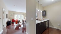 This single-floor residence offers a thoughtfully designed open-concept layout that seamlessly connects the kitchen, dining, and living areas. The kitchen features dark espresso cabinetry, white countertops, stainless steel appliances including a full-size refrigerator and dishwasher, an undermount sink, and elegant pendant lighting. A pass-through window connects the kitchen to the dining area, enhancing the open feel. Rich hardwood flooring flows throughout the main living spaces, adding warmth and visual continuity.

The dining area accommodates a full dining table and benefits from natural light, while a round decorative mirror adds depth to the room. The living room is bright and inviting, centered around French doors that open to a private balcony, allowing abundant natural light to fill the space.

The bedrooms are carpeted for comfort, with the primary bedroom featuring large windows with outdoor views, soft neutral tones, and ample space. A second bedroom provides additional versatility. The bathroom is finished with large-format tile flooring, dark vanity cabinetry with a sink and mirror, and a shower-tub combination. Throughout the residence, warm beige walls and consistent finishes create a cohesive, modern aesthetic.