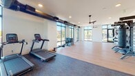 Located at 143 E White St in Rock Hill, SC, this single-floor amenity lounge is designed with a modern industrial aesthetic that blends bold style with functional recreation. The space is anchored by deep navy-blue walls, polished concrete floors, and a dramatic oversized photographic mural depicting industrial machinery, lending the interior a distinctive, urban character.

The main area features a regulation ping pong table set atop a geometric patterned area rug, positioned beneath a sculptural multi-arm pendant light fixture. Large floor-to-ceiling windows and an oversized garage-style door flood the space with natural light and provide views of an outdoor area, creating a seamless indoor-outdoor connection.

A dedicated lounge zone offers channeled navy velvet seating, cognac leather accent chairs, and a shuffleboard table, all set against the striking industrial mural wall. A wall-mounted television is positioned nearby, alongside a small beverage and snack bar area with open shelving. An additional seating cluster with a round table provides a more intimate setting. Curated artwork and layered lighting complete the sophisticated, community-focused ambiance of this well-appointed gathering space.