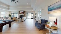 Located at 101 Grand Bahama Dr in Conway, SC, this single-story clubhouse is a well-appointed community amenity space designed with a clean, modern aesthetic. Light hardwood flooring flows throughout, tying together the various functional areas into a cohesive and inviting environment.

The expansive main lounge serves as the heart of the space, featuring a striking stone fireplace flanked by wall-mounted televisions, comfortable seating arrangements, and a pool table — creating a versatile gathering area suited for both relaxed socializing and recreation. Large glass sliding doors open directly to an outdoor patio, flooding the interior with natural light and providing seamless indoor-outdoor connectivity.

The kitchen area is outfitted with granite countertops, white shaker cabinetry, a subway tile backsplash, stainless steel appliances, pendant lighting, and a central island with a sink — ideal for community events and casual use. Adjacent dining areas feature large windows and a sliding glass door that frame views of the surrounding landscape, enhancing the sense of openness.

A dedicated business center provides a row of computer workstations along a granite-topped counter, offering a productive workspace for residents. The fitness center, accessible through full-length glass French doors, is equipped with cardio and strength training equipment, accented by bold blue walls and ample natural light.