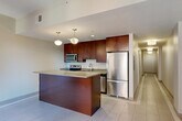 Located at 1249 Griswold St in the heart of Detroit, MI, this one-bedroom, one-bathroom residence offers a thoughtfully designed single-floor layout with a clean, modern aesthetic throughout. The open-concept kitchen, dining, and living area serves as the centerpiece of the unit, featuring rich dark-wood cabinetry, stainless steel appliances including a refrigerator, electric range, and built-in microwave, and a generously sized peninsula with a light quartz-style countertop that doubles as a breakfast bar. Pendant lighting adds a contemporary touch above the kitchen island. Light-toned tile flooring flows through the main living areas, contributing to a bright and airy atmosphere. The bedroom is carpeted for comfort and includes a sliding-door closet, with neutral wall tones creating a calm, restful environment. Additional closets throughout the unit provide ample storage. The bathroom is well-finished with tile flooring featuring a mosaic border detail, a glass-enclosed walk-in shower, a long vanity with an undermount sink, and a mirrored medicine cabinet with sleek strip lighting. A dedicated laundry area and a connecting hallway complete the practical and efficient floor plan of this Detroit residence.