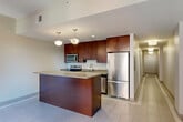 Located at 1249 Griswold St in the heart of Detroit, MI, this one-bedroom, one-bathroom residence offers a thoughtfully designed single-floor layout with a clean, modern aesthetic throughout. The open-concept kitchen, dining, and living area serves as the centerpiece of the unit, featuring rich dark-wood cabinetry, stainless steel appliances including a refrigerator, electric range, and built-in microwave, and a generously sized peninsula with a light quartz-style countertop that doubles as a breakfast bar. Pendant lighting adds a contemporary touch above the kitchen island. Light-toned tile flooring flows through the main living areas, contributing to a bright and airy atmosphere. The bedroom is carpeted for comfort and includes a sliding-door closet, with neutral wall tones creating a calm, restful environment. Additional closets throughout the unit provide ample storage. The bathroom is well-finished with tile flooring featuring a mosaic border detail, a glass-enclosed walk-in shower, a long vanity with an undermount sink, and a mirrored medicine cabinet with sleek strip lighting. A dedicated laundry area and a connecting hallway complete the practical and efficient floor plan of this Detroit residence.