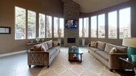 This thoughtfully designed single-floor space makes a striking first impression with its open, airy layout and carefully curated finishes throughout. The centerpiece of the living area is a dramatic curved bay of tall, narrow windows that flood the room with natural light and offer views of the surrounding landscape. A floor-to-ceiling stacked-stone fireplace anchors the space, paired with a wall-mounted flat-screen TV, creating a warm and inviting focal point. The living area accommodates generous seating arranged around a glass-topped coffee table, all set atop large-format tile flooring with an elegant patterned area rug. Soaring ceilings contribute to an expansive sense of volume throughout.

A wide, open transition leads into the kitchen, which is appointed with rich, dark espresso cabinetry extending to the ceiling, stainless steel appliances including a refrigerator, range, and dishwasher, and a dark countertop with an undermount sink. Recessed lighting illuminates the workspace efficiently, while a window above the sink brings in additional natural light. A connecting hallway with tile flooring and recessed lighting provides access to additional areas of the space, further highlighting the cohesive, neutral color palette of warm taupe and crisp white trim that unifies the entire interior.