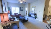 Located at 3511 Birchfield Ct in Hope Mills, North Carolina, this single-story home offers a well-designed, comfortable living environment. The living room serves as the heart of the home, showcasing plush wall-to-wall carpeting, neutral-toned walls, and generous natural light streaming in through multiple windows. A ceiling fan with a light fixture provides both airflow and ambient lighting, contributing to the room's airy, welcoming atmosphere. The space is thoughtfully laid out to accommodate generous seating arrangements, with clear sightlines that connect the living area to adjacent rooms. A decorative console table with a mirror adds an elegant touch to one wall, enhancing the sense of depth and style. The open flow between the living room and the bedroom beyond suggests a cohesive, accessible floor plan well-suited for everyday living. Tasteful greenery and decor accents add warmth throughout. The home's single-floor layout makes it practical and easy to navigate, while its neutral palette and carpeted floors create a cozy, move-in-ready environment. Overall, this Hope Mills residence combines comfort, functionality, and understated style in a welcoming single-level design.