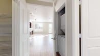 Located at 6715 E Union Ave in Denver, CO, this well-appointed studio offers a thoughtfully designed single-floor layout that maximizes functionality and style. Light wood-tone flooring runs throughout, creating a warm and cohesive aesthetic across every space.

The open-concept kitchen and living area serves as the heart of the unit. The kitchen is outfitted with rich, dark wood cabinetry extending to the ceiling for ample storage, complemented by granite countertops, a tile backsplash, and a full suite of stainless steel appliances including a refrigerator, electric range, built-in microwave, and dishwasher. The living area benefits from generous natural light streaming through large windows and a set of French doors, lending the space an airy, open ambiance with views of the surrounding Denver cityscape.

The hallway connects to a dedicated closet housing a stacked washer and dryer, adding everyday convenience. The walk-in closet features built-in wire shelving and hanging rods, providing organized storage space. Crown molding trims the main living area, adding a refined architectural detail.

The bathroom is finished with the same dark wood vanity and granite countertop found in the kitchen, a large wall mirror, globe vanity lighting, and a shower-tub combination — maintaining a consistent, modern design language throughout the unit.