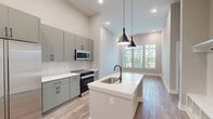 Located at 2127 Morton St in Charlotte, NC, this one-bedroom, one-bathroom unit offers a thoughtfully designed layout with modern finishes throughout. The single-level floor plan makes efficient use of its space, seamlessly connecting the kitchen and living area in an open-concept arrangement.

The kitchen is a standout feature, equipped with sleek gray cabinetry extending to the ceiling, a white quartz island with an undermount sink, stainless steel appliances including a French door refrigerator and built-in microwave, and a subway tile backsplash. Pendant lighting with matte black fixtures adds a contemporary touch above the island, complementing the black hardware found throughout the unit.

The living area flows naturally from the kitchen and is brightened by recessed lighting and warm-toned luxury vinyl plank flooring, which runs consistently throughout the unit. The bedroom offers generous natural light through large windows with outdoor tree views, high ceilings, and direct access to the bathroom. The bathroom features marble-look tile flooring and walls, a glass-enclosed walk-in shower, a gray vanity with black hardware, and an adjoining walk-in closet with built-in shelving. Neutral gray walls and clean white trim create a cohesive, modern aesthetic throughout.