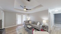 This single-floor, three-bedroom, two-bathroom residence offers a thoughtfully designed layout that balances comfort and functionality. The living room serves as the heart of the home, showcasing a distinctive tray ceiling with crown molding, a ceiling fan, and light hardwood-style flooring. French doors flood the space with natural light and provide access to an outdoor area, creating a seamless indoor-outdoor connection.

Adjacent to the living room, the dining area features the same hardwood-style flooring and is anchored by a stylish globe chandelier, making it an inviting space for gatherings. The kitchen is outfitted with white shaker-style cabinetry, white countertops, and stainless steel appliances, including a range and over-the-range microwave.

The primary bedroom offers plush carpeting, ample space, and access to an en-suite bathroom featuring a soaking tub with a tiled surround and chrome fixtures. The secondary bedrooms are carpeted and include ceiling fans and windows that bring in natural light. The second full bathroom features marble-look tile flooring, a tub-shower combo, and a white vanity, maintaining the home's clean, modern aesthetic throughout.